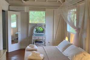A bedroom with a bed, a small white fireplace, and a view of greenery outside. - Villa Ti' Colibri – Creole Villa with Pool Near the Beach (Saint-François)