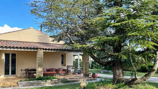 Ein Haus mit Terrasse, Sitzgelegenheit im Freien, einem großen Baum und einem Garten.