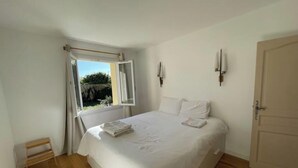 Ein Schlafzimmer mit Bett, Fenster, Tür und einer kleinen Holzablage.