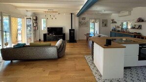 Eine moderne Küche mit Kochinsel, ein Essbereich mit Sofa und ein Wohnzimmer mit Fernseher und Bücherregal.