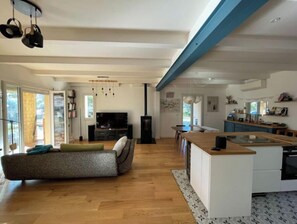 Eine moderne Küche mit Kochinsel, ein Essbereich mit Sofa und ein Wohnzimmer mit Fernseher und Bücherregal.
