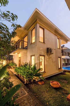 A two-story building with a balcony, a satellite dish, and a small garden area with plants and a brick pathway. - Staymaster Casa Mancurad 3BR Villa  (Vagator)