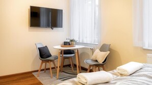 A hotel room with a bed, two chairs, a small table, a flat-screen TV, and a window with sheer curtains. - Malila Premium Apartments Traugutta (Kraków)