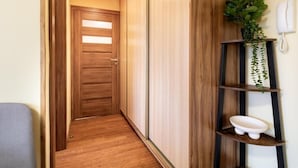 A hallway with a wooden door, a plant on a shelf, and a telephone on the wall. - Malila Premium Apartments Traugutta (Kraków)