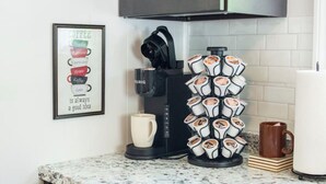 A kitchen with a coffee maker, a mug, and a coffee cup holder with multiple cups. - Coastal Gem - Charming 3BR Home, Steps to Beach! (Warwick)