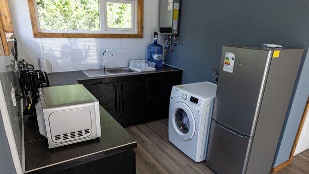 A compact kitchen with a washing machine, a refrigerator, and a microwave. - cabañas entre sauces (Coyhaique)
