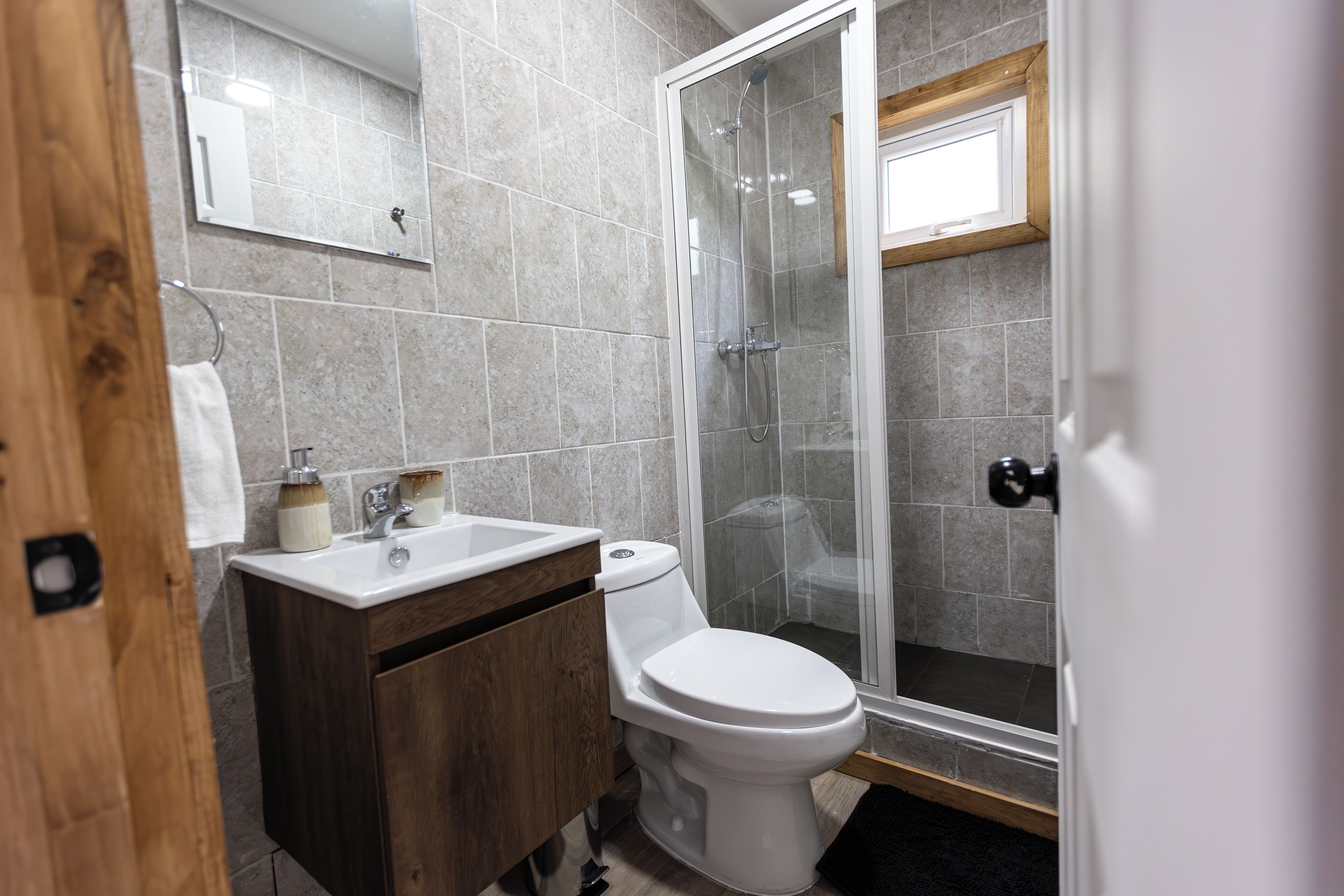 A bathroom with a shower, toilet, sink, and wooden cabinet.