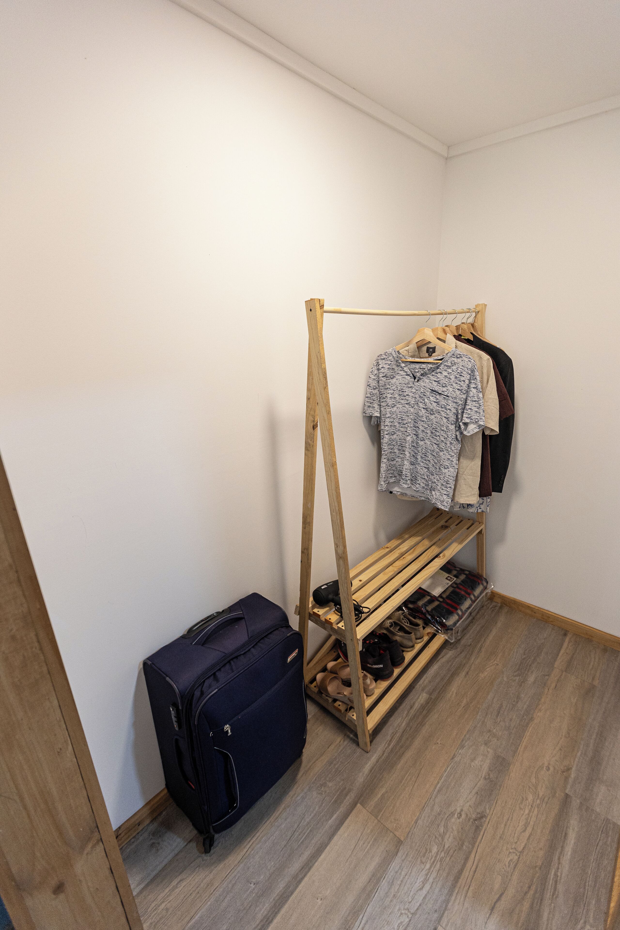 Una habitación con un zapatero de madera, un perchero y una maleta.