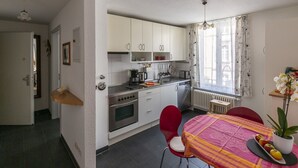 Een kleine keuken met witte kastjes, een fornuis en een eethoek met een tafel en stoelen.