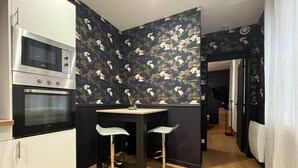 A kitchen with a microwave, oven, two bar stools, and a patterned wallpaper. - Charming apartment in the heart of the city center – 2 guests (Angers)