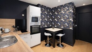 A compact kitchen with a microwave, oven, and sink, a small table with two chairs, and a dark patterned wall. - Charming apartment in the heart of the city center – 2 guests (Angers)