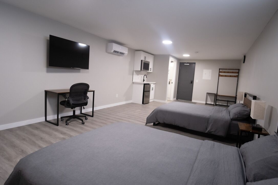 A room with two beds, a desk, a chair, a TV, a microwave, and a door.
