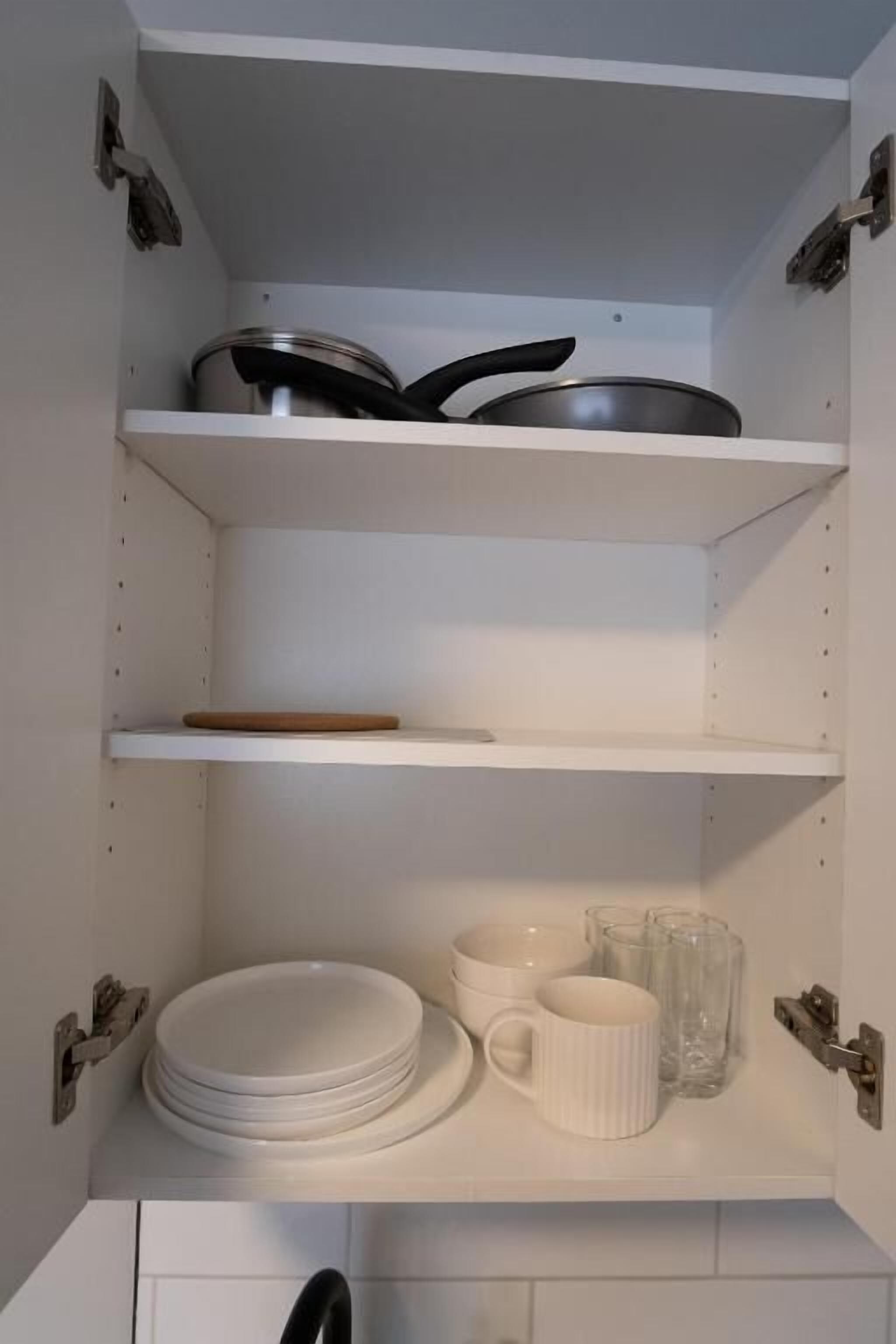 A kitchen with white cabinets, a stove, and a shelf with plates, bowls, and cups.