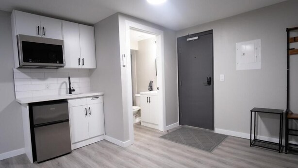 A modern kitchen with white cabinets, a stainless steel refrigerator, and a microwave. - CK Motel (Chatham)