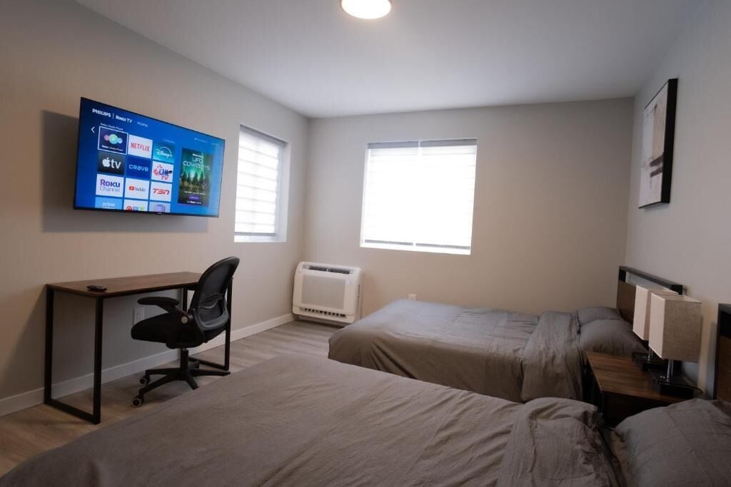 Une chambre d’hôtel avec deux lits, un bureau, une chaise, un téléviseur fixé au mur et une fenêtre.