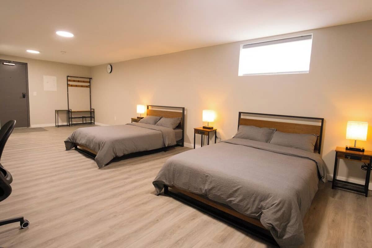 Habitación de hotel con dos camas, un escritorio, una silla, un reloj y una ventana.