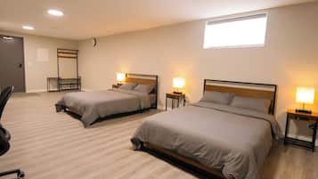 A hotel room with two beds, a desk, a chair, a clock, and a window.
