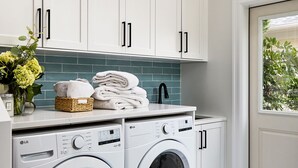 A laundry room with two front-loading washing machines, a sink, and a basket of folded towels on a counter. - Historical suite for writers and hikers (Toscana)