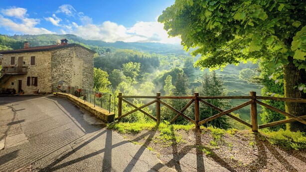 A stone building with a paved road and a wooden fence. - Historical suite for writers and hikers (Toscana)
