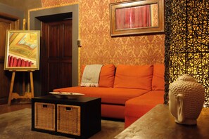 Une pièce avec une porte en bois, un canapé orange, une petite table avec des paniers et une statue de Bouddha.