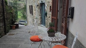 A stone building with a patio, a table with chairs, and a car parked outside. - Historical suite for writers and hikers (Toscana)