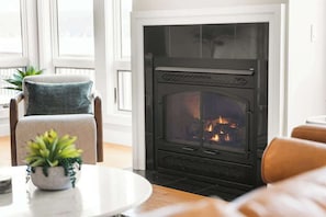 A living room with a fireplace, a sofa, a chair, and a table with a plant.