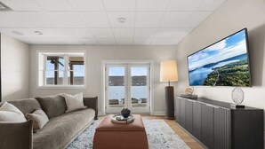 A living room with a sofa, a coffee table, a TV, and a view of a body of water through a window.