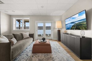 A living room with a sofa, a coffee table, a TV, and a view of a body of water through a window.