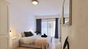Un dormitori amb llit, taules de nit, un mirall, una finestra amb cortines i una planta.