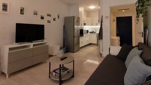 Un saló amb televisió, sofà, taula de centre i una cuina al fons.