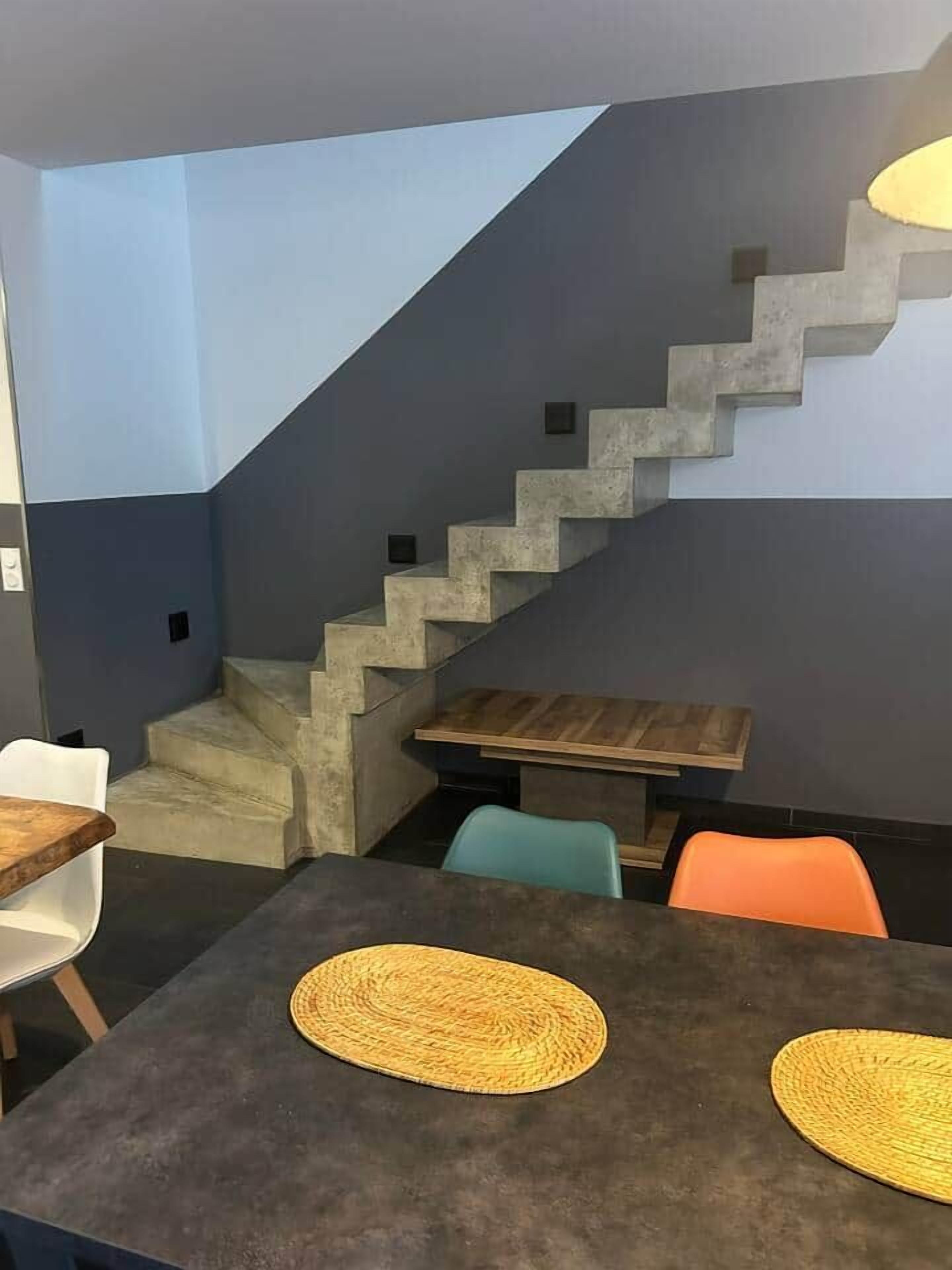 Een modern interieur met een trap, een eethoek met tafels en stoelen, en een klein houten tafeltje.