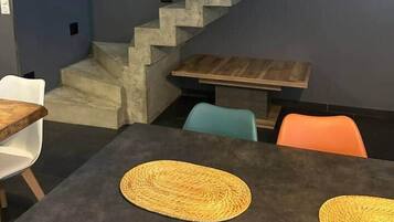 Een modern interieur met een trap, een eethoek met tafels en stoelen, en een klein houten tafeltje.