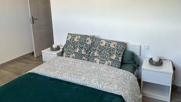 Een slaapkamer met een bed, twee nachtkastjes, een nachttafel, een kunstwerk in een lijst en een deur.