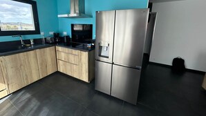 A modern kitchen with a stainless steel refrigerator, wooden cabinets, a black countertop, and a window with a view. - Seaside house adjoining the beach Leucate La Franqui (Leucate)