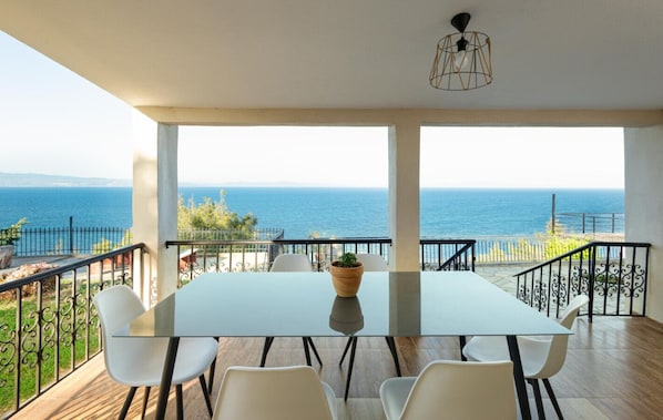 A dining area with a table and chairs, a potted plant, and a view of the sea.