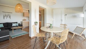 Ein modernes Wohnzimmer mit einer Couch, einem Couchtisch, Korbstühlen, einem Esstisch und einer Pendelleuchte.