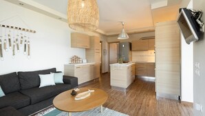 Ein modernes Wohnzimmer mit Sofa, Couchtisch und einer Küchenzeile mit Holzschränken und eingebautem Backofen.