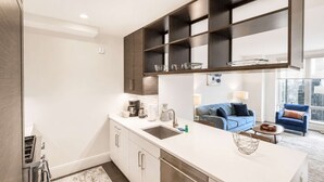 Eine moderne Küche mit einer zentralen Kochinsel, eingebauten Regalen über der Arbeitsfläche und Blick in einen Wohnbereich mit einem blauen Sofa und Stadtansicht.