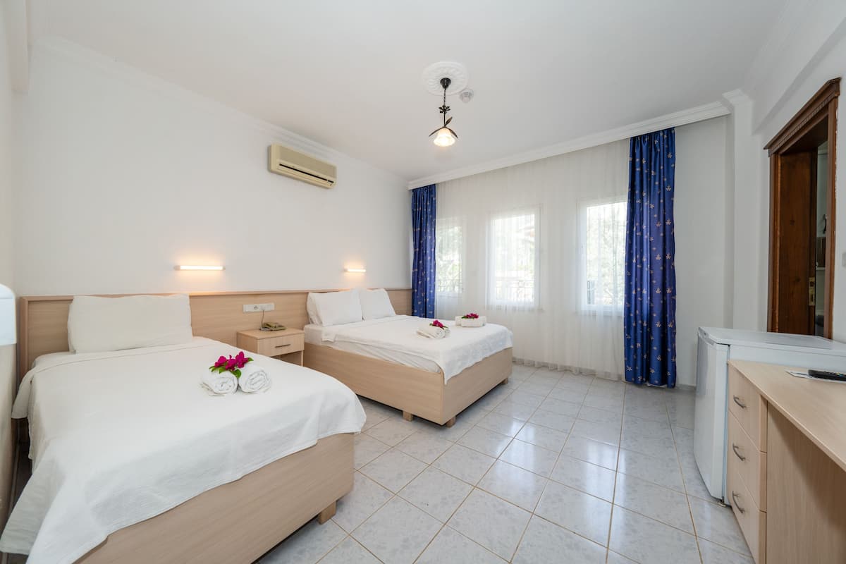 Habitación de hotel con dos camas, un escritorio, un refrigerador y un ventilador de techo.