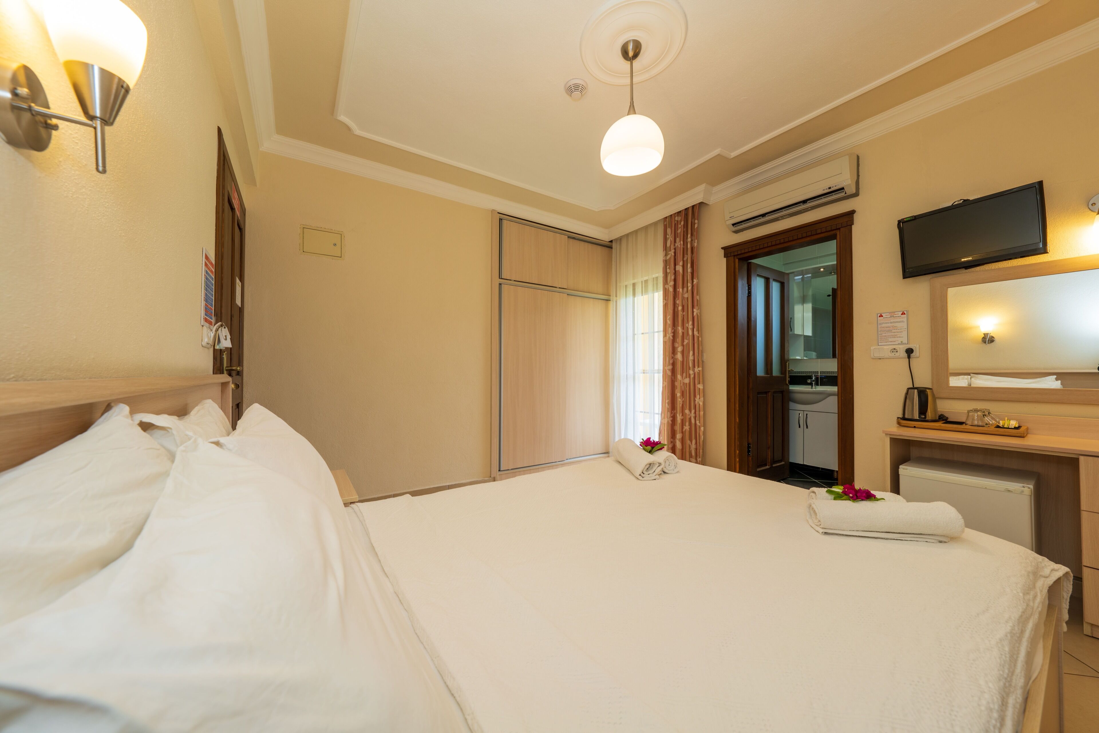 Une chambre d’hôtel avec un lit, un bureau doté d’un téléviseur à écran plat, un miroir et une salle de bain visible à travers une porte ouverte.