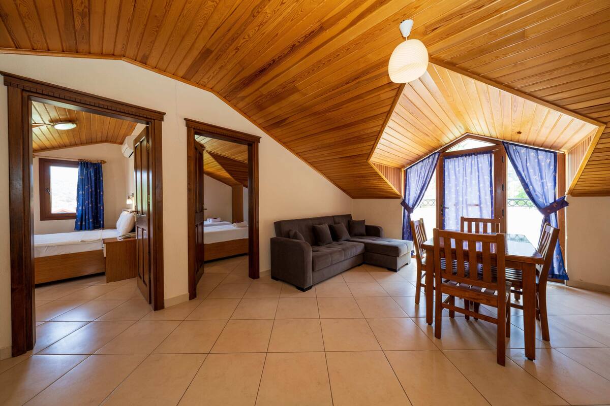 Una habitación con techo de madera, un sofá, una mesa de comedor con sillas y una ventana con cortinas.