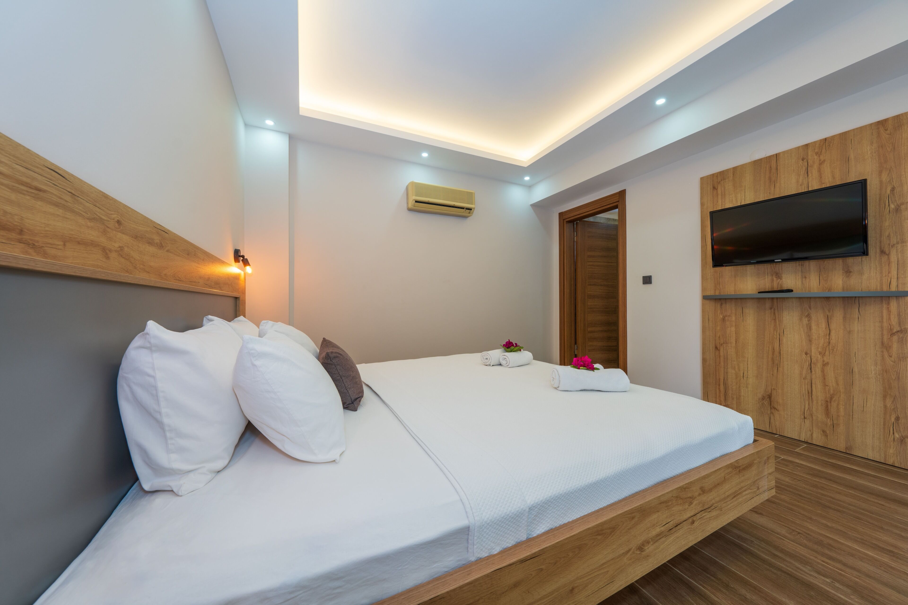 A modern bedroom with a bed, built-in TV, and recessed ceiling lighting.