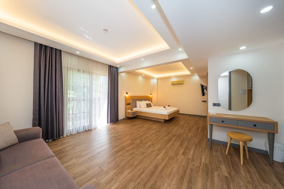 Una habitación de hotel moderna con piso de madera, una cama con cabecera de madera, un escritorio con espejo y un sofá.