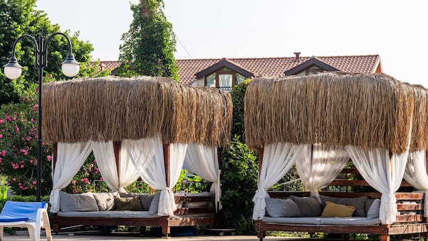A poolside area with two thatched-roof cabanas, a lounge chair, and a clear blue pool. - Gokcen Hotel & Aparments (Fethiye)