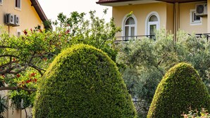A courtyard with stone paving, neatly trimmed hedges, and a building with a tiled roof. - Gokcen Hotel & Aparments (Fethiye)