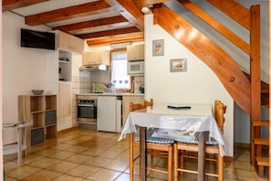 A kitchen with wooden beams, a dining table with chairs, and a TV mounted on the wall. - Gite Riesling – Kaysersberg Vignoble, Mountain View, Private Terrace & Parking (Kaysersberg Vignoble)