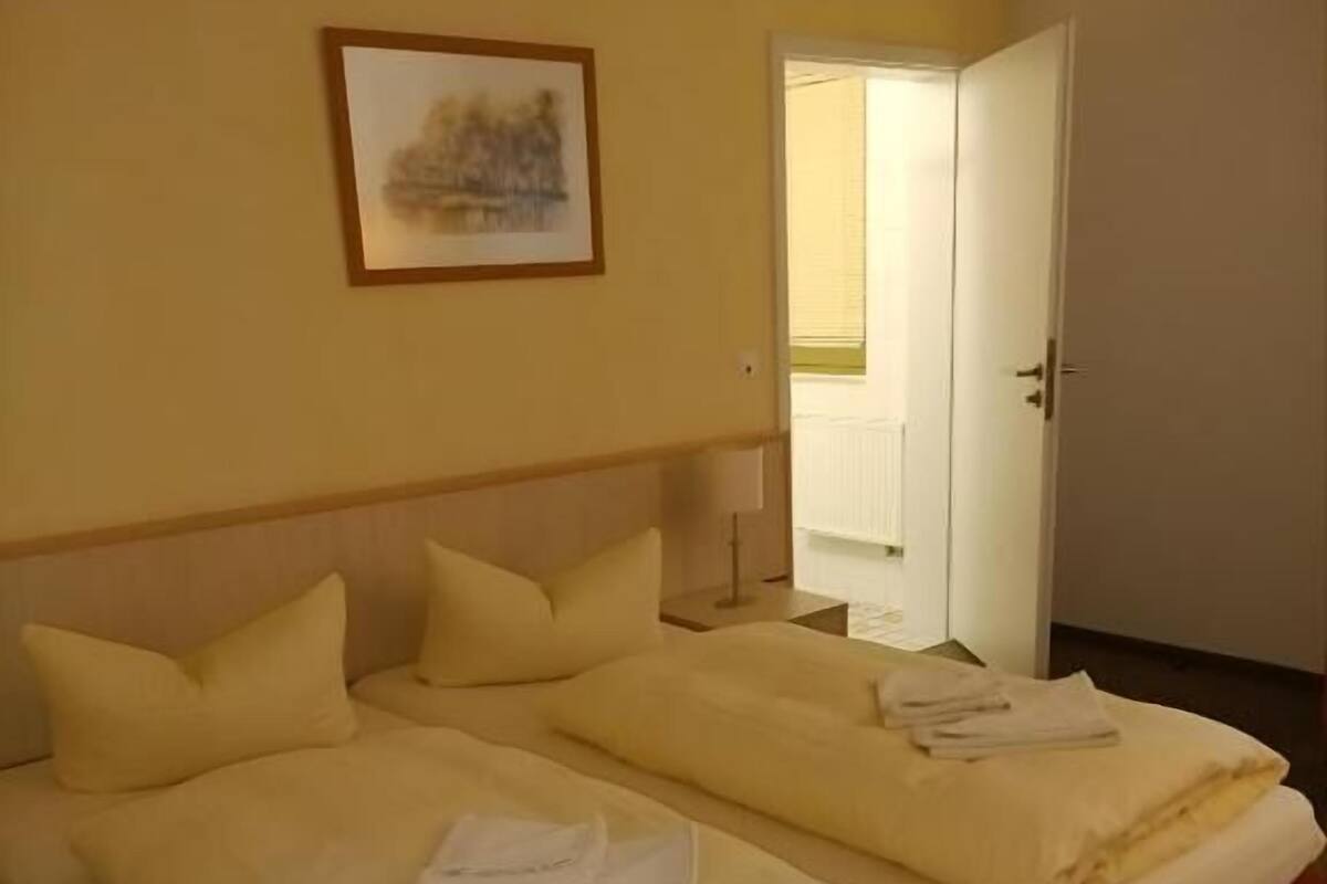 Ett hotellrum med två sängar, en tavla på väggen och en dörr som leder till ett badrum.