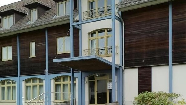 A multi-story building with a central staircase, balconies, and a small garden area. - Pension am Seeberg (Zeschdorf)