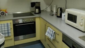 A compact kitchen with a stove, oven, microwave, and a coffee maker. - Pension am Seeberg (Zeschdorf)