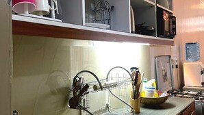 Uma cozinha com pia, escorredor de louça e diversos utensílios de cozinha nas prateleiras.